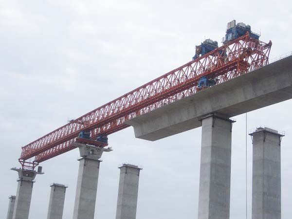 Launching gantry carried on tall piers above a concrete box-girder deck, with the main truss extended over the next span.
