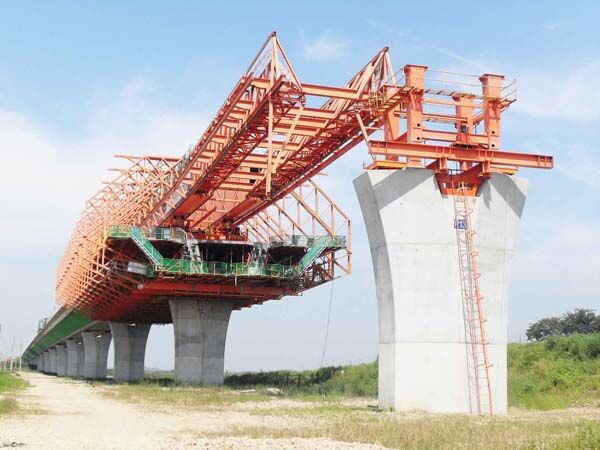 Overhead movable scaffolding system at a pier, with the main truss carried above deck level and the casting form and working platforms suspended beneath it.