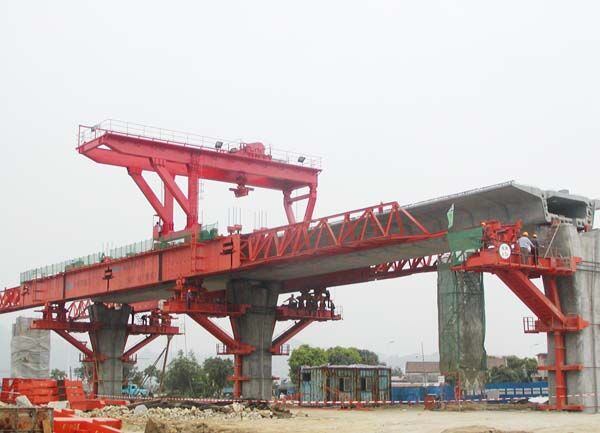 Launching gantry supported on its legs across two piers, with the overhead crane beam above the main truss and a completed deck span ahead.