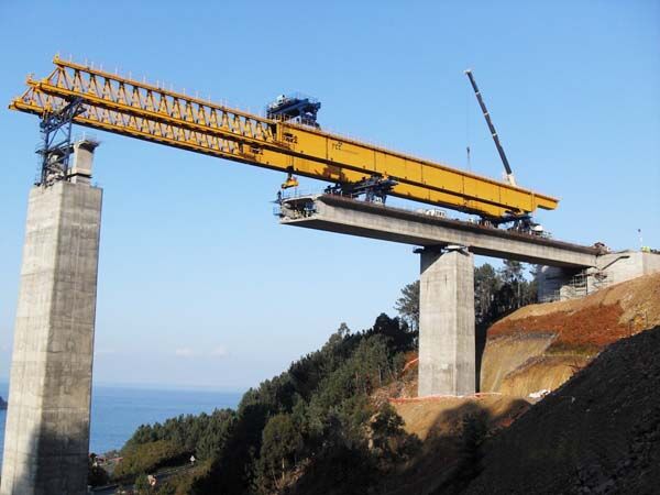 Launching gantry supported on its legs across two piers, with the overhead crane beam above the main truss and a completed deck span ahead.