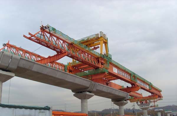 Launching gantry carried on tall piers above a concrete box-girder deck, with the main truss extended over the next span.