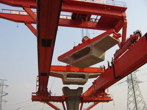 Launching gantry above a bridge pier lifting a precast concrete box segment, with a second segment already positioned beneath the gantry.