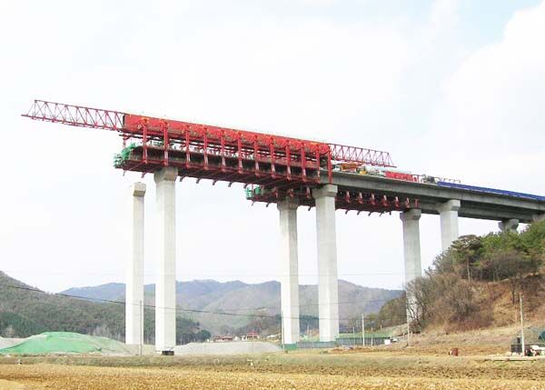 Overhead movable scaffolding system working on tall piers, the main truss above deck level and the formwork carriage suspended below it.