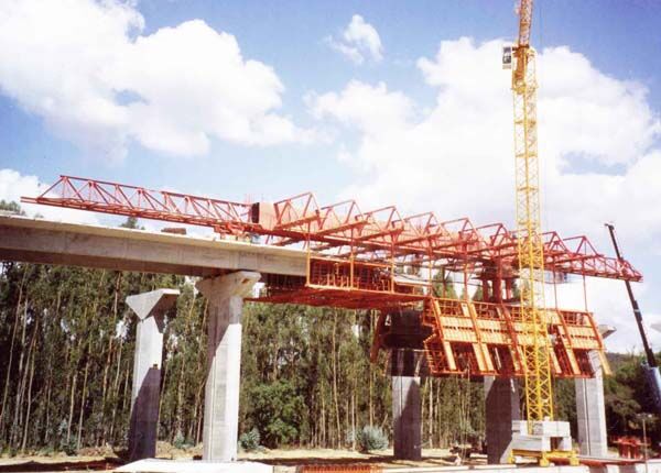 Overhead movable scaffolding system with the outer formwork panels swung open below the main truss, alongside a completed deck span.